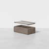 A rectangular wooden storage box with a detached lid hovering above it, shown on a smooth, light gray surface against a plain white background.