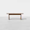A simple wooden bench with a flat rectangular seat and three legs, set against a plain white background.