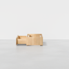 A minimalist wooden storage unit with two open drawers placed on a light grey floor against a plain white background.