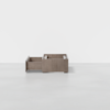 A minimalist wooden storage box with two compartments, one open and one closed, sits on a smooth, light gray floor against a plain white background.
