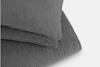 Close-up of folded, textured dark gray bedding or blankets with a subtle crinkled pattern, set against a light background.