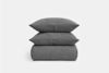A neatly stacked set of two gray textured pillows sitting on top of a matching folded gray blanket, all set against a plain white background.