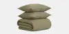 Two khaki-colored pillows are stacked on top of a matching, neatly folded quilt or comforter, all set against a plain white background.