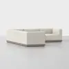 A modern, L-shaped sectional sofa with light beige upholstery and a low wooden base, set against a plain, light gray background.
