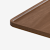 A close-up of the corner of a rectangular wooden tray with rounded edges and a shallow groove along the border, set against a plain white background.