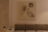 A modern living room with a beige sofa, a white side table, and abstract geometric art in neutral tones hanging on a cream-colored wall above the sofa.
