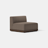 A modern, armless brown upholstered lounge chair with a low wooden base, placed on a light gray floor against a plain white background.