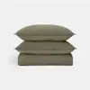 A neatly stacked bedding set in olive green, featuring two pillows placed on top of a folded quilt, all with a subtle square quilted pattern, against a plain white background.