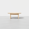 A minimalist, light wood round coffee table with three legs, set against a plain white background.