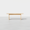 A simple, light wood rectangular table with clean lines, placed on a smooth gray floor against a plain white background.