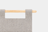 A close-up of a wooden rod threaded through two loops of thick, light gray felt fabric against a plain white background.