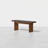 A modern wooden bench with a black cushioned seat, set against a plain white background. The bench has simple, clean lines and sturdy rectangular legs.