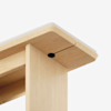 Close-up view of a light wood table corner, showing the tabletop secured to the leg with a visible black screw, against a plain white background.