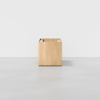 A minimalist, light wood storage cube with an open top and a divider inside, placed on a smooth, light gray floor against a plain white background.