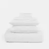 A stack of neatly folded white bedding, including two pillows, sheets, and a comforter, arranged on a plain white background.