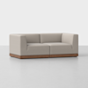 A modern, light beige upholstered sofa with square armrests and backrest, featuring a wooden base, sits on a light grey floor against a plain white background.