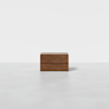A minimalist wooden rectangular box with two horizontal grooves, placed on a smooth, light gray surface against a plain white background.