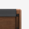 Close-up of the corner of a wooden bed frame with a dark gray fabric-covered headboard, showcasing smooth, rounded wood edges and visible metal fasteners.