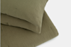 Two olive green, textured fabric pillows are stacked on top of each other, shown against a plain white background. The pillows have a soft, quilted appearance with a subtle square pattern.