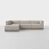A modern, L-shaped sectional sofa with light beige upholstery and a low wooden base, set against a plain white background on a light gray floor.