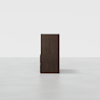 A dark brown wooden cabinet viewed from the side, standing alone on a light gray floor with a plain white background.