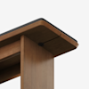 Close-up view of the corner of a wooden table with a dark trim on the top edge, featuring clean lines and a minimalist design against a plain white background.