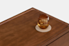 A brown glass with a light brown drink sits on a round coaster on a wooden surface, against a plain white background.