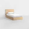 A single wooden bed with a headboard, made of light-colored wood, is placed against a plain white wall. The bed is neatly made with white sheets and a white pillow. The floor is smooth and light gray.