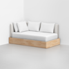 A modern daybed with a light wood base, white mattress, beige upholstered backrest, and four white pillows, placed in a minimalistic room with white walls and a light gray floor.