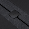 Close-up of a black textured fabric strap secured by a metal clasp with the word THUMA engraved on it, set against a dark background.