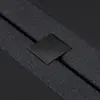 Close-up of a black textured fabric strap secured by a metal clasp with the word THUMA engraved on it, set against a dark background.
