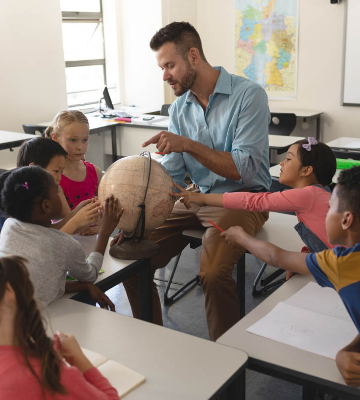 Children gathering around teacher pointing at a globe