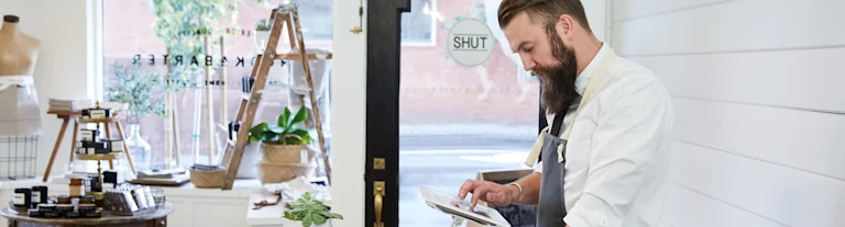 Small business owner reviewing tablet behind checkout counter