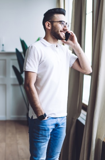 man standing at window while on phone