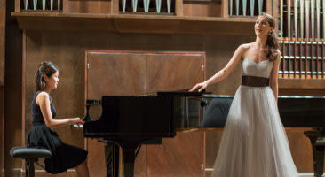 girl playing the piano with performer singing