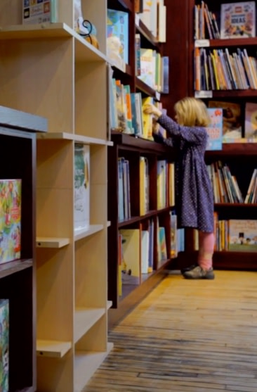 Child looks at books on bookshelf at Blue Bunny Books & Toys