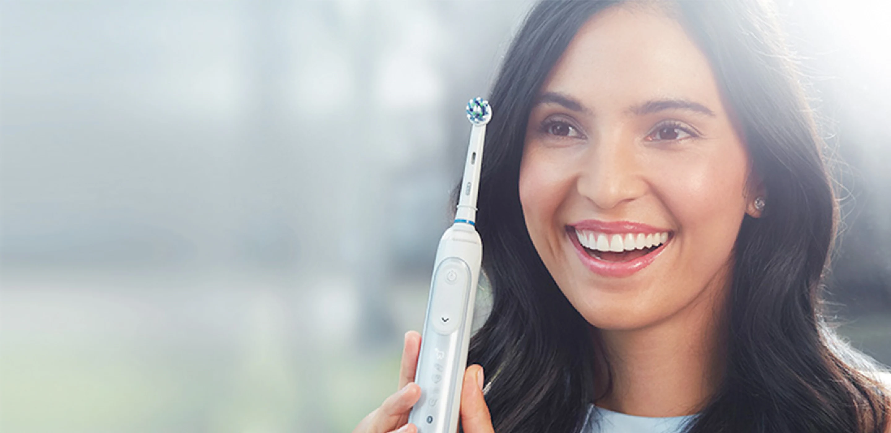 Woman smiling and holding an Oral-B iO rose quartz electric toothbrush