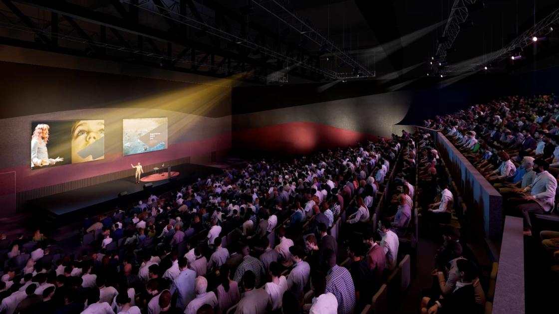 Render of inside the theatre at Nyaal Banyul Convention and Event Centre. Rows of people in a theatre formation facing a stage with a presenter and two large screens on it. 