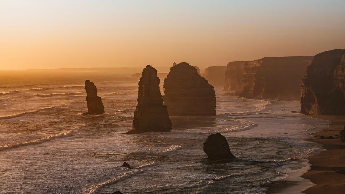 Twelve Apostles along the cliff side as the sun sets from the far left of the image.