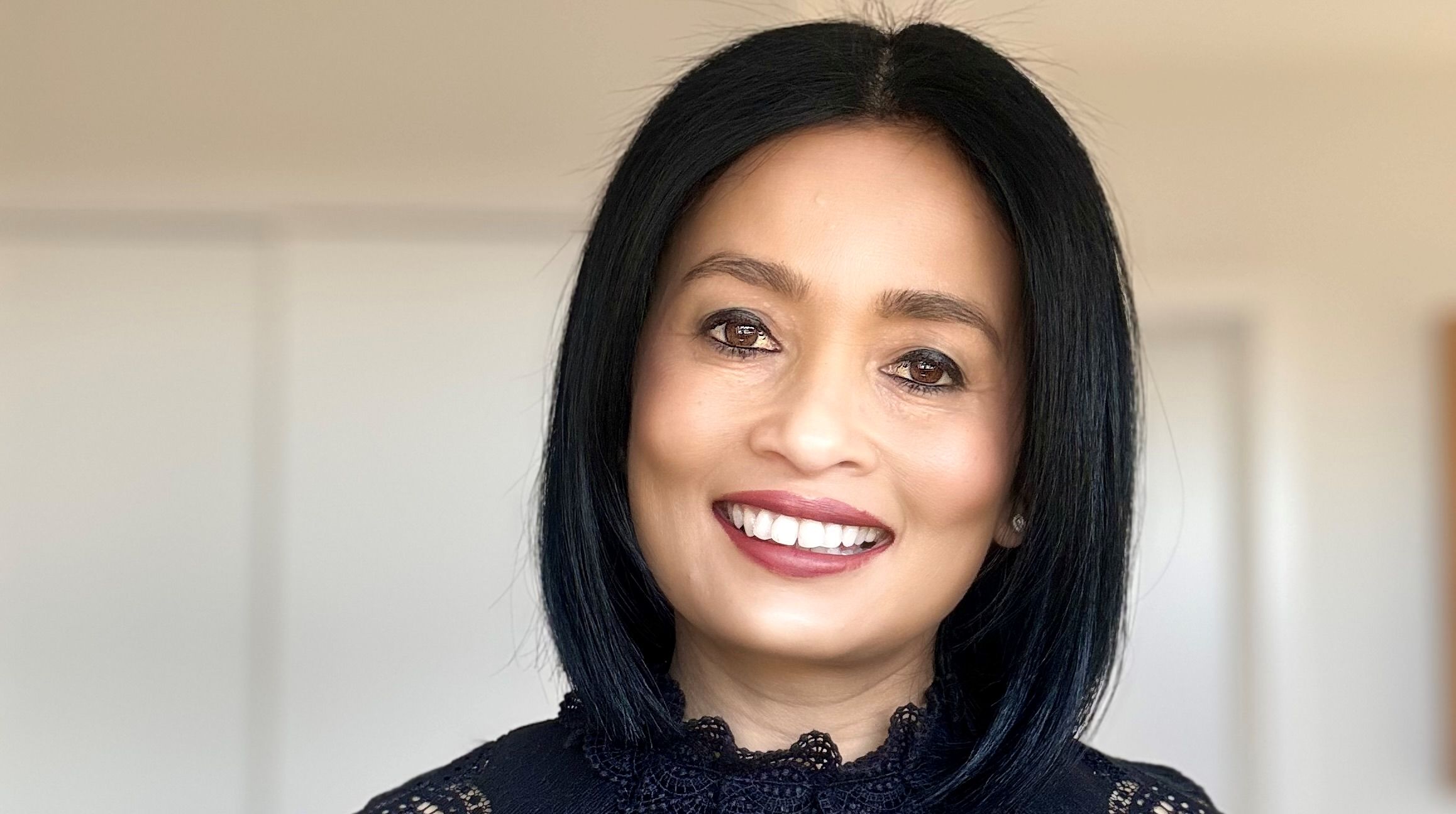 A close up headshot of Sujata Stead - a woman with black hair smiling wearing a red top. 