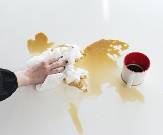 Foto på en spilld kaffekopp och en hand som torkar upp kaffet med papper.