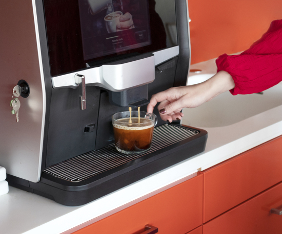 Foto på en kaffemaskin med en hand som sträcker sig efter en kaffekopp.