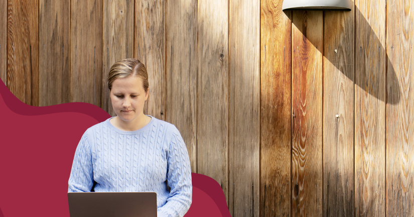 På bilden syns en kvinna i blå stickad kofta med en laptop framför sig. Bakom henne syns ett träplank.