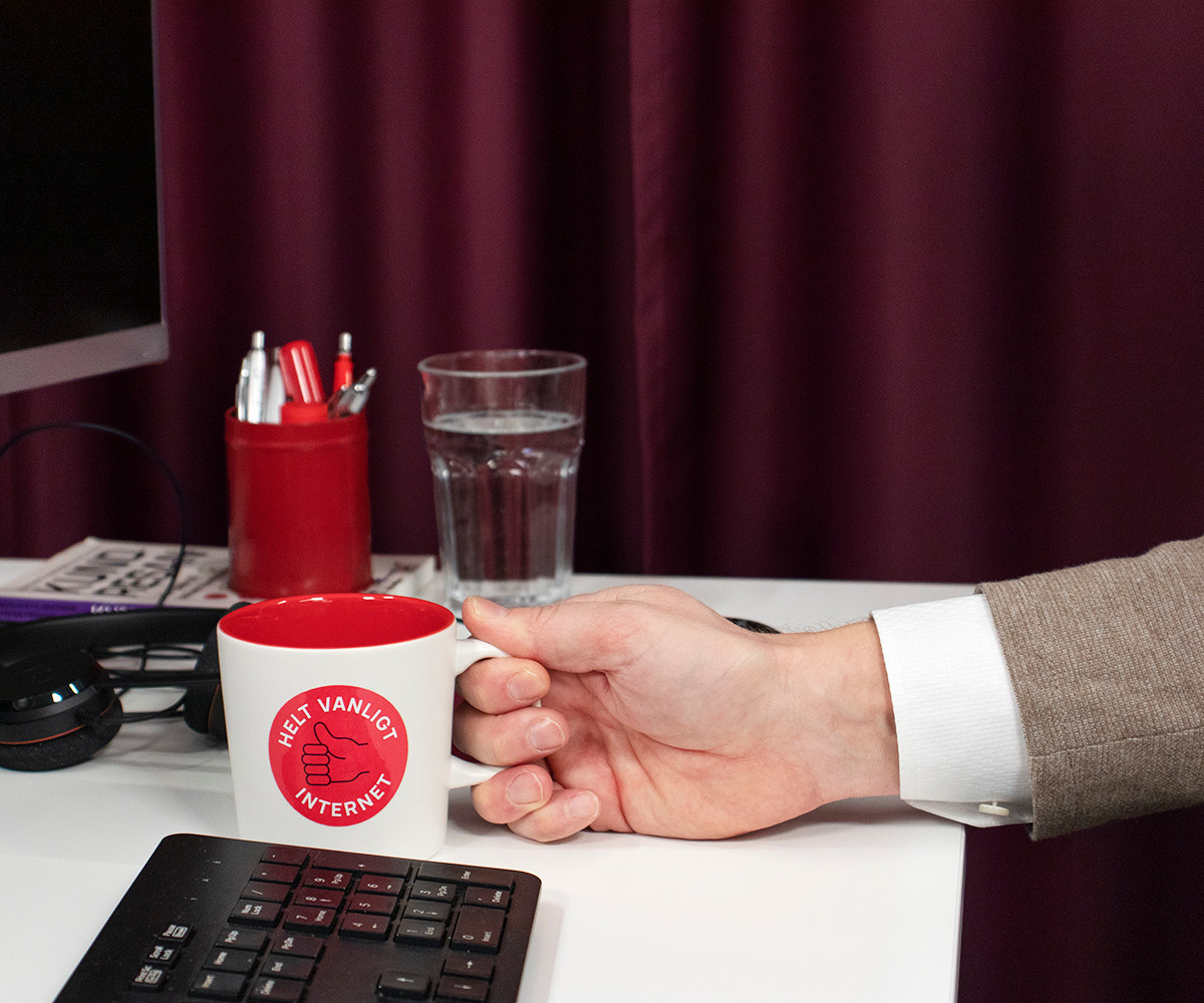 Foto på ett skrivbord med en hand som håller i en kaffekopp.