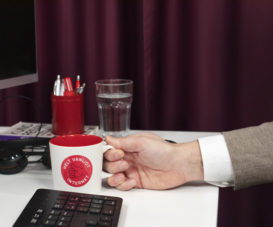 Foto på ett skrivbord med en hand som håller i en kaffekopp.