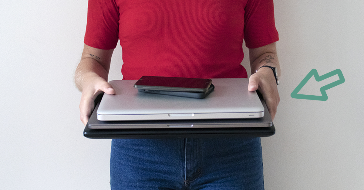 Bilden föreställer en person i röd tröja och jeans som håller tre staplade laptops i händerna framför sig.