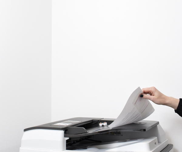 Foto på en hand som tar ett papper från en kopiator på ett kontor.