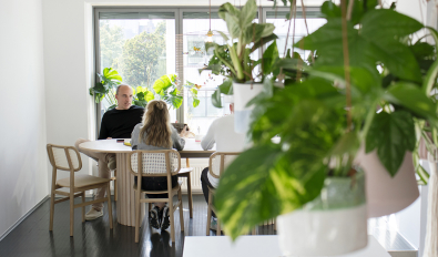 Foto på personer som sitter i lunchrummet och samtalar med växter i förgrunden. 
