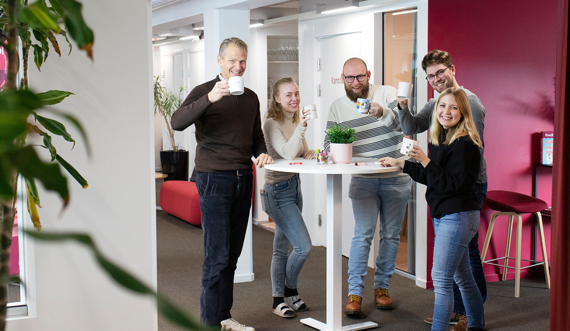 Foto på medarbetare på Bredband2 som ler och står vid ett högt bord och dricker kaffe