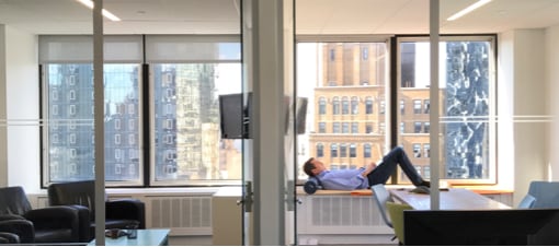 View into two conference rooms with someone lying on the windowsill lost in thought, and midtown buildings visible through the windows 